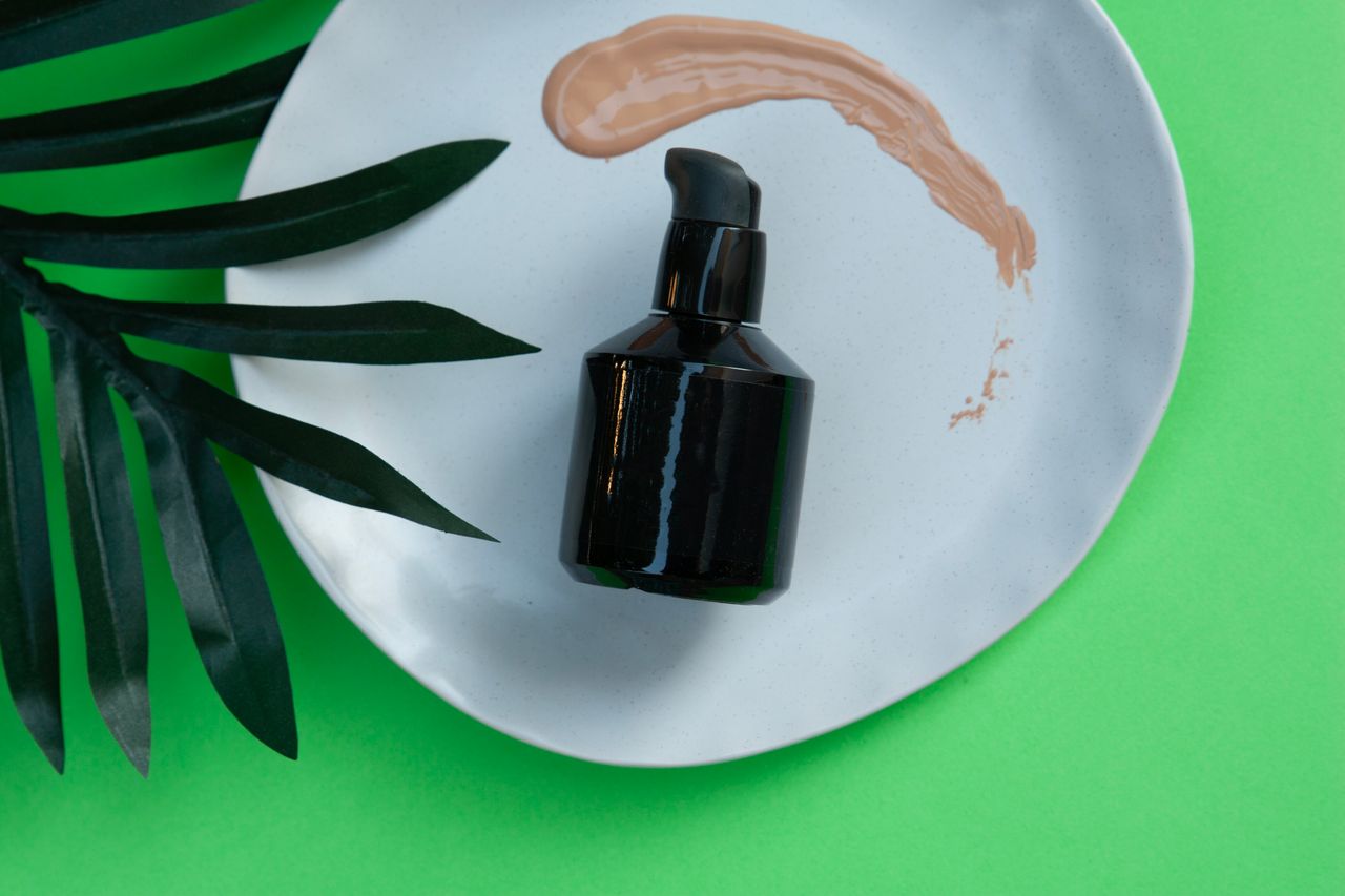 Rutina bio pentru îngrijirea părului: Cum treci la produse fără sulfați și siliconi Black skincare pump bottle on a white plate with green leaf and makeup smear.