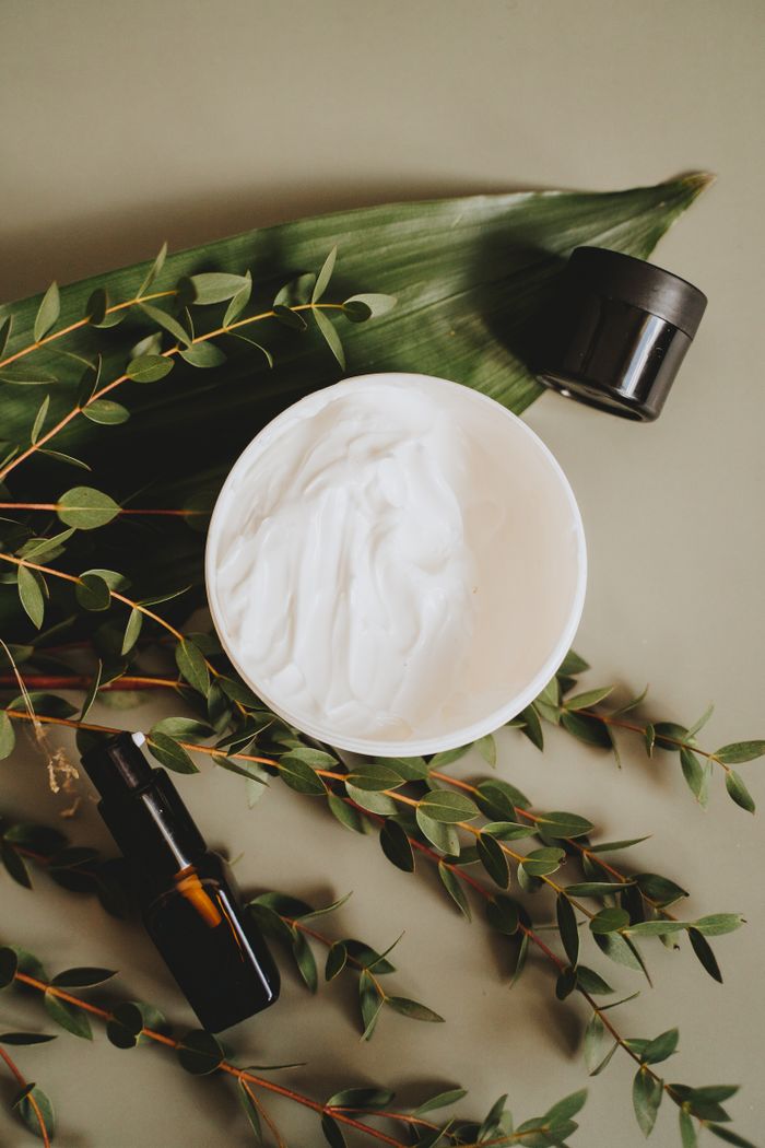 Cum construiești o rutină de skincare bio pentru pielea sensibilă: Ghid pas cu pas Overhead view of skincare cream with botanical leaves and dropper bottles for natural beauty products.